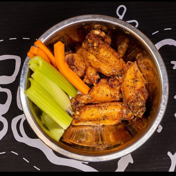 A metal bowl filled with crispy chicken wings, celery sticks, and carrot sticks.