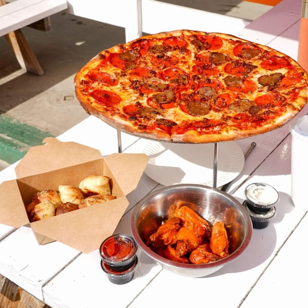 Dough Momma Pizzeria's pepperoni and sausage pizza, garlic knots, and buffalo wings on a white table.