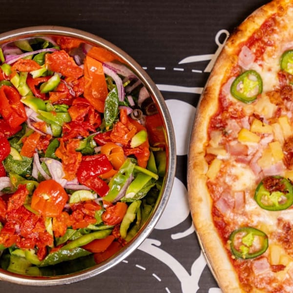 A Dough Momma Pizzeria pizza with pineapple and jalapeños next to a fresh salad.