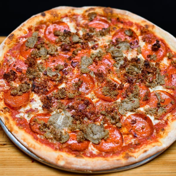 Dough Momma Pizzeria's meat lover's pizza, topped with pepperoni, sausage, and bacon, on a wooden table.