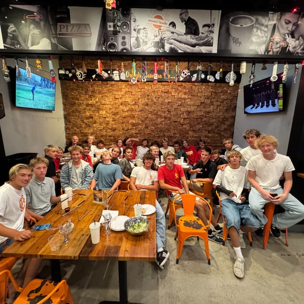 A large group of young men gathered around wooden tables at Dough Momma Pizzeria.