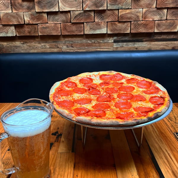 Dough Momma Pizzeria's pepperoni pizza and a pitcher of beer on a wooden table.