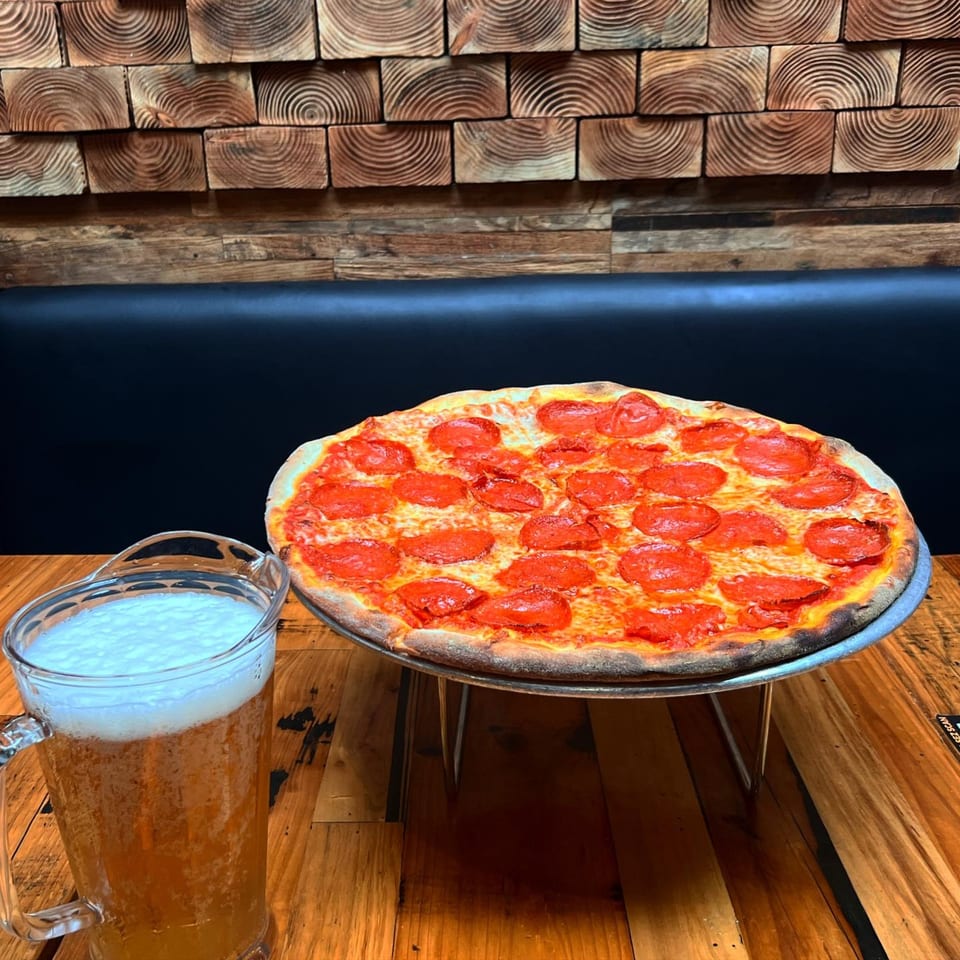 Dough Momma Pizzeria's pepperoni pizza and a pitcher of beer on a wooden table.