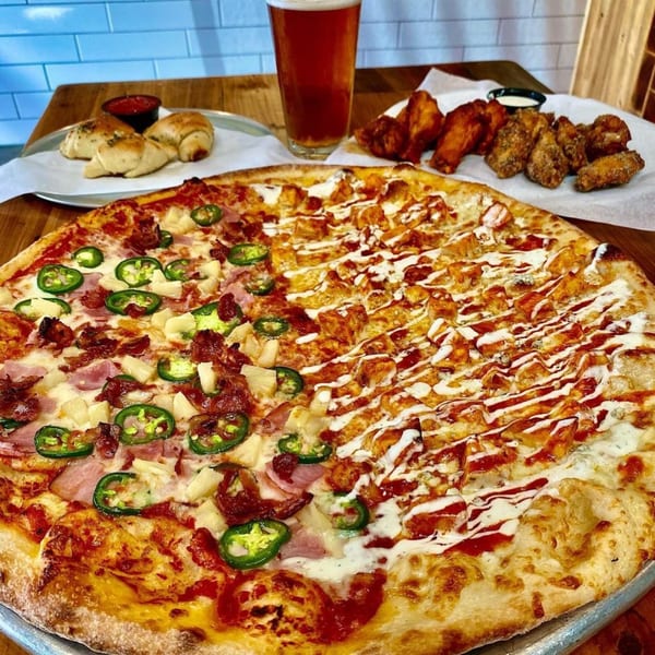 A Dough Momma Pizzeria feast: half Hawaiian, half buffalo chicken pizza, wings, garlic knots, and beer.