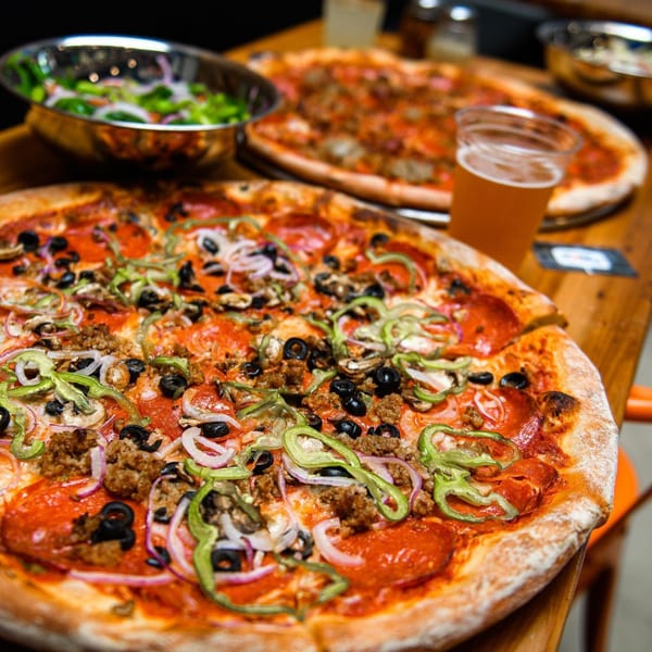 Two Dough Momma Pizzeria pizzas with various toppings, a side salad, and a beer on a wooden table.