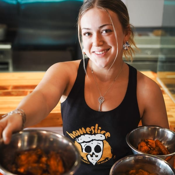 Smiling Dough Momma Pizzeria employee in a black tank top holding bowls of chicken wings.